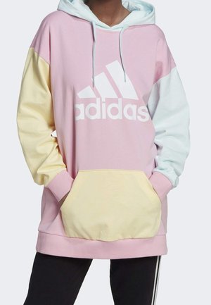 Lichtroze hoodie met capuchon, met gele en blauwe kleurblokken op de mouwen, een groot wit adidas-logo en een buidelzak aan de voorkant. Zachte stoftextuur.
