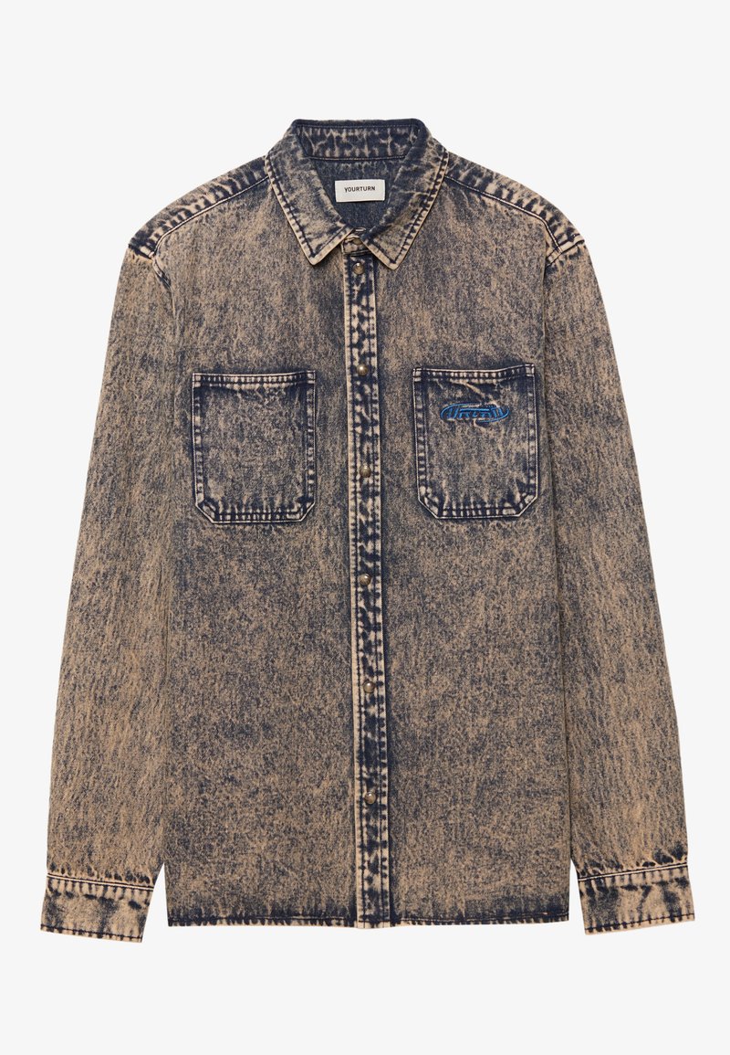 Chemise en denim bleu clair et beige délavé, avec deux poches sur la poitrine, fermeture à boutons, et un motif texturé sur l'ensemble.
