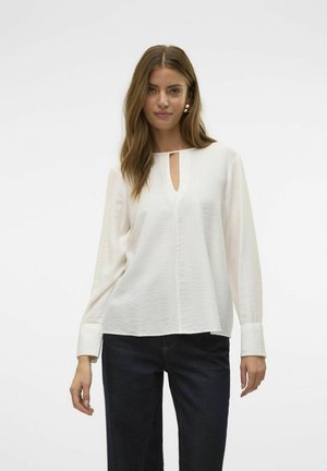 Witte blouse met lange mouwen en een keyhole-halslijn, zachte textuur en rechte zoom. Gekleed met donkerblauwe jeans. Geen zichtbare patronen of hardware.
