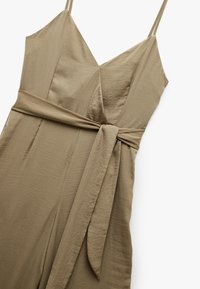 Khaki-Overall mit tiefem V-Ausschnitt, dünnen Trägern und gebundenem Taillenzug. Hergestellt aus glattem, leichtem Stoff mit einem sanften Glanz.