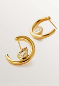 Pendientes de metal en tono dorado con un diseño curvado que presenta un acento de cristal transparente en forma de pera en el centro. El acabado pulido realza el brillo.