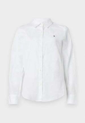 Chemise blanche à manches longues boutonnée avec col classique et petit logo Tommy Hilfiger sur la poitrine gauche.