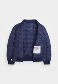 Námořnická modrá prošívaná bunda s žebrovaným límcem, manžetami a spodním lemem, rozepnutá, aby odhalila značkové štítky Polo Ralph Lauren uvnitř.