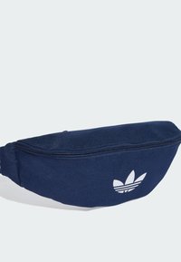 Navy blue fabric fanny pack with a zipper closure, featuring a white Adidas trefoil logo on the front, and a smooth, textured surface.