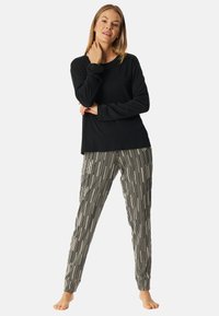 Zwarte langemouwtop gecombineerd met zwart-wit gestreepte pyjamabroek met kleine steraccenten. Zacht materiaal, relaxte pasvorm, elastische manchetten.