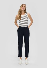 Marineblauwe op maat gemaakte broek met opgerolde boorden, gecombineerd met een wit tanktop met marineblauwe strepen. Model draagt witte sneakers.