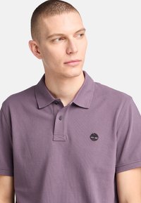Polo tričko s krátkým rukávem v levandulové bavlně s texturovaným povrchem, s dvouknoflíkovým zapínáním a černým vyšitým logem na hrudi.