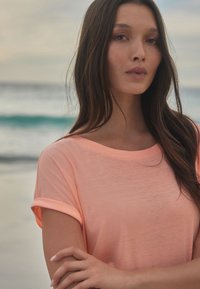 Kerge, lühikeste varrukatega t-särk ere korallis, lai kaelus ja rullitud varrukad. Pehme, poolläbipaistev kangas kerge tekstuuriga.