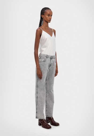 Hvid satin v-hals top parret med høj talje, lysegrå denim jeans. Model iført blanke burgunderrøde hælede støvler.
