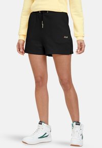 Shorts de sport noirs avec une ceinture élastique, un cordon de serrage et le logo Fila. Assortis à des baskets montantes blanches avec des accents verts.