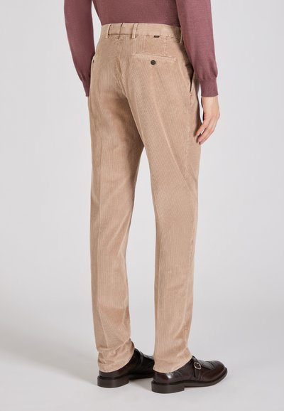 Beżowe spodnie w korduroy w prostym kroju, z dwoma tylnymi kieszeniami i subtelną teksturą w prążki, zestawione z ciemnymi skórzanymi butami.