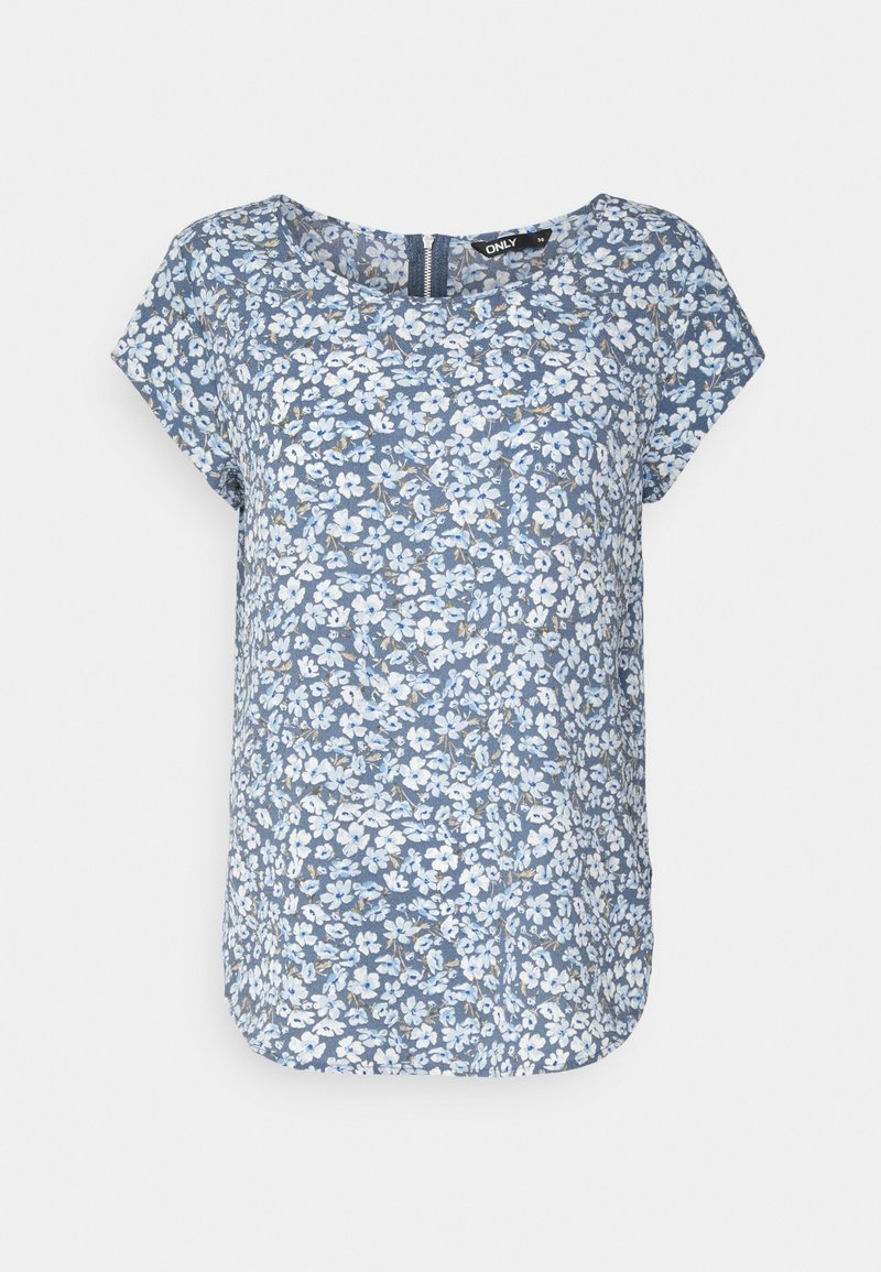 Blouse bleue à manches courtes avec imprimé floral blanc et col rond, avec fermeture éclair visible dans le dos.