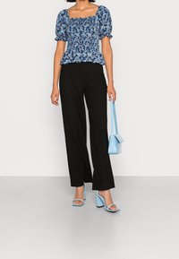 Blus med blommönster i blått och puffärmar, matchad med svarta ribbade vida byxor. Accessoarer inkluderar en ljusblå handväska och klackar.