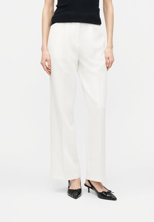 Woman wearing white wide-leg trousers and black sleeveless top, paired with black pointed slingback heels.