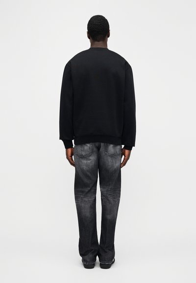 Schwarzer Pullover mit langen Ärmeln und dunkelgraue Jeans. Der Pullover hat einen Rundhalsausschnitt; die Jeans besitzen eine verwaschene Textur mit Gesäßtaschen.