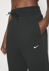 Svarta Nike-mjukisbyxor har en dragsko i midjan, sidofickor och en liten vit logotyp på vänster lår. Mjukt tyg med en avslappnad passform.