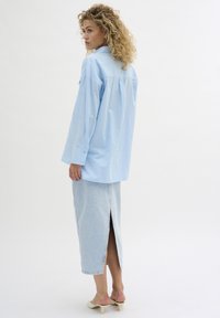 Light blue button-up shirt with a relaxed fit, paired with a light denim skirt featuring a back slit, and beige heeled sandals.