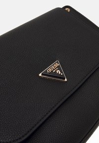 Black faux leather handbag with textured surface, featuring a triangular gold and black "GUESS" logo plaque on the front.