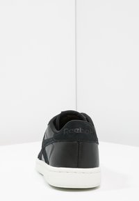 Baskets en cuir noir avec des accents en daim doux, semelle blanche et col rembourré. Présente un logo sur le talon et un design bas.