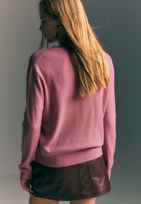 Różowy kaszmirowy sweter o luźnym kroju, z prążkowanymi mankietami i dołem. Noszony z brązową skórzaną spódnicą. Gładka faktura i prosty design.