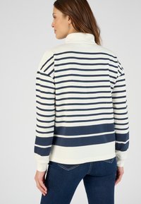 Suéter rayado en crema y azul marino, con un collar alto, puños acanalados y un corte holgado. Textura suave y patrón de rayas horizontales.