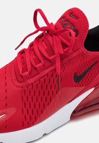 Red athletic shoe with a breathable mesh upper, black accents, and flat laces. Features a padded collar and a visible air cushioning unit.