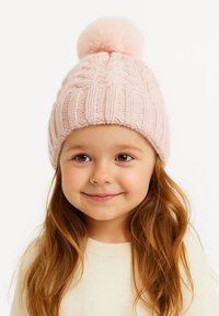 Gaiši rozā adīta cepure ar teksturētu kabeļu rakstu un pūkainu pom-pom virsotnē. To valkā bērns ar gariem, viļņotiem matiem.