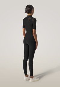 Svart passande träningsklädesset bestående av en kortärmad topp med hög krage och leggings. Märkbara texturerade detaljer på ärmarna och sidorna.