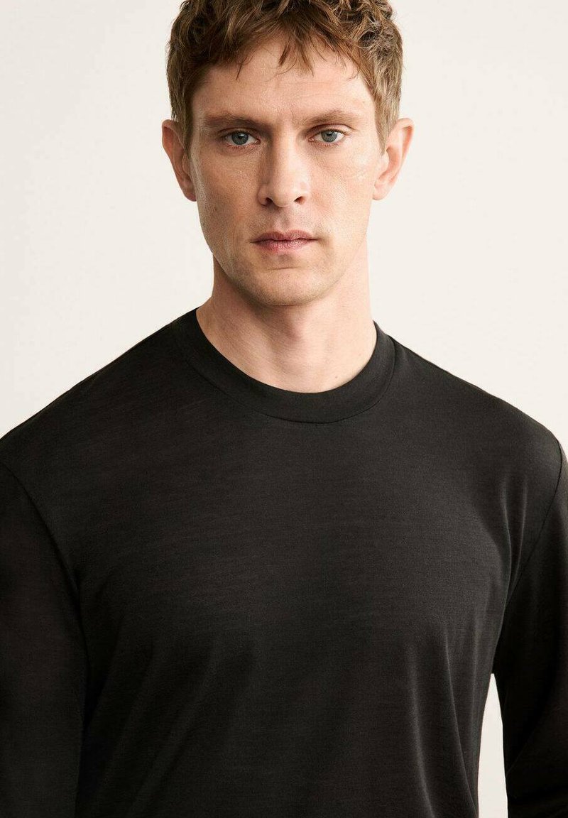 Black long-sleeve shirt made from soft fabric. Features a crew neckline and a smooth texture, suitable for layering or casual wear.
