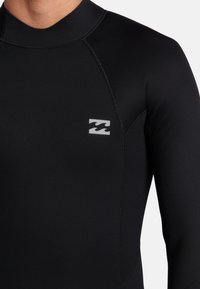 Traje de neopreno negro de manga larga. Hecho de material elástico, con costuras planas y un acento de logo gris en el pecho.