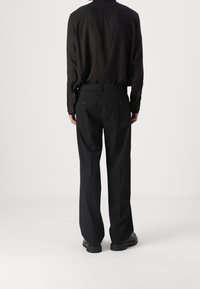Schwarzes Langarmshirt mit geknöpften Manschetten, kombiniert mit schwarzen Hosen im geraden Schnitt und zwei Gesäßtaschen. Glatte Stofftextur.
