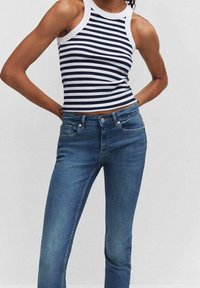 Person wearing a sleeveless navy and white striped crop top with high-waisted blue jeans, standing with hands behind back.