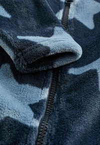 Fleece-takki, jossa on tummansininen ja vaaleansininen tähtikuvio, jossa on sileä vetoketju ja pehmeä, teksturoitu fabrikki.