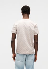 Φωτεινό μπεζ κοντομ άνικο μπλουζάκι με υφασμάτινο μοτίβο κύκλων. Το ύφασμα φαίνεται λείο, με κλασικό στρογγυλό λαιμό.