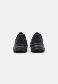Chaussures de sport noires avec une tige en tissu texturé, un col rembourré et une semelle en caoutchouc. Présente un logo discret au niveau du talon et des accents sur la semelle intermédiaire.