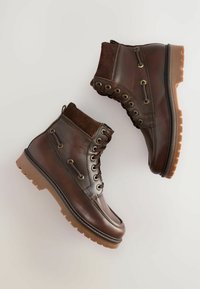 Botas de tobillo de cuero marrón con empeine de ante, ojales de latón y una suela de goma marrón con un diseño de tracción robusto.