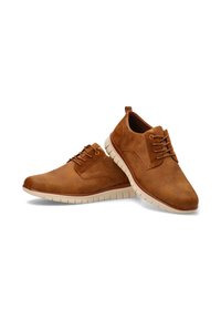 Zapatos de cuero sintético marrón con una textura suave, diseño de cordones, forma curva y suelas de goma blancas. Presenta detalles de costura simples.