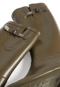 Bottes de pluie en caoutchouc marron avec une finition brillante, dotées d'une sangle à boucle et d'un logo en relief. Design large avec des semelles texturées pour une meilleure adhérence.