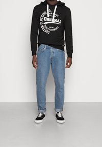 Felpa nera con stampa bianca, abbinata a jeans in denim azzurro chiaro, risvoltati alle caviglie. Completa il look un paio di sneakers nere con suola bianca.