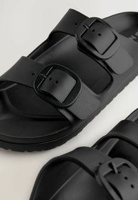 Sorte sandaler med to justerbare stropper med firkantede spænder, lavet af tekstureret materiale, med en formet fodseng og flad sål.