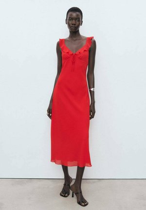 Red midi dress with a fitted bodice, ruffled straps, and a tie detail at the neckline. Sheer hem detail. Worn with black heeled sandals.