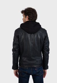 Černá kožená bunda s černou kapucí, s hladkým povrchem, přiléhavým střihem a podrobným prošíváním na rukávech a zádech.