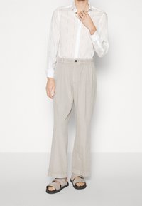 Lekka biała koszula o subtelny wzorze, w połączeniu z luźnymi beżowymi spodniami i czarnymi sandałami ze stanikami.