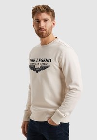Bežna majica s kapuljačom z ribanim ovratnikom i manžetami. Ima crni grafični print z krili in besedilom "PME LEGEND AMERICAN CLASSIC." Ozek kroj.