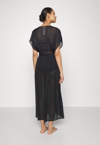 Vestido negro transparente con mangas cortas y anchas, cintura ajustada y una falda fluida. La tela es ligera y ligeramente transparente.