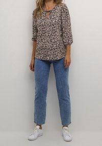 Blusa a righe nera e beige con maniche a tre quarti, scollatura a chiave e vestibilità morbida, abbinata a jeans blu chiaro a gamba dritta e sneakers bianche.