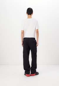 Schwarze Cargo-Hosen mit mehreren Seitentaschen, lockerer Passform und passendem Bund. Getragen mit einem schlichten weißen T-Shirt und schwarzem Schuhwerk.