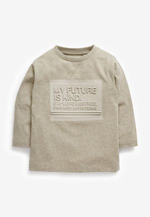 Chemise beige à manches longues pour tout-petit avec un patch en relief comportant le texte "MON AVENIR EST BIENVEILLANT. EXPLOREZ & SOYEZ LIBRE. DECOUVREZ DE NOUVELLES AVENTURES."