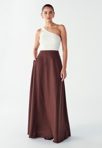 Geribbelde witte top met één schouder, gecombineerd met een lange, bruine, vloeiende rok. Gladde textuur met een strakke, aansluitende tailleband voor een op maat gemaakte pasvorm.