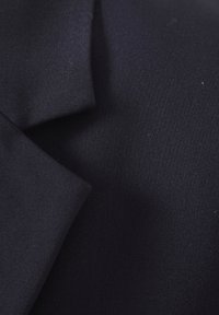 Gros plan sur un tissu bleu marine foncé avec un revers plié, montrant la texture fine tissée d'une veste de costume.